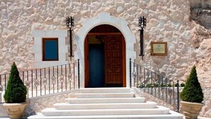 Un edificio de piedra con puerta de madera, una escalera y dos plantas en macetas.