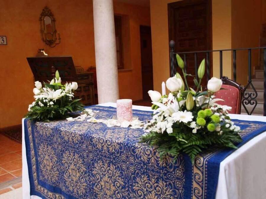 A table with a blue patterned tablecloth, two floral arrangements, and a candle.