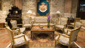 Un salón formal con alfombra estampada, sillones decorados, una mesa central con un florero y un gran emblema en la pared.