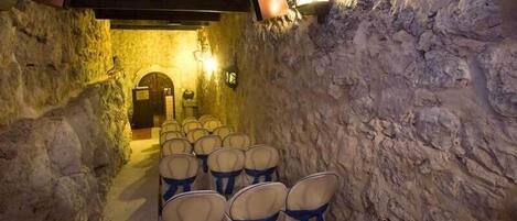 Un étroit couloir en pierre, bordé de rangées de chaises, et une porte en bois au fond.