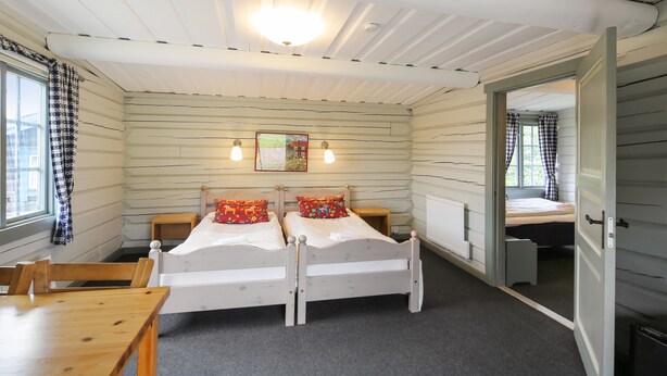 A room with two beds, a wooden table, and a window with curtains. - Dala Wärdshus (Rattvik)