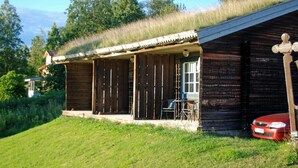 A rustic wooden cabin with a thatched roof, a small porch with chairs, and a car parked nearby. - Dala Wärdshus (Rattvik)