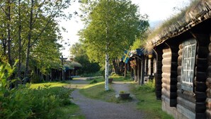 A rustic log cabin with a thatched roof, a gravel path leading to it, and a flagpole with a flag. - Dala Wärdshus (Rattvik)