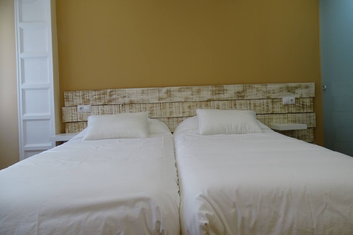 A double bed with white bedding in a room with yellow walls and a wooden headboard.