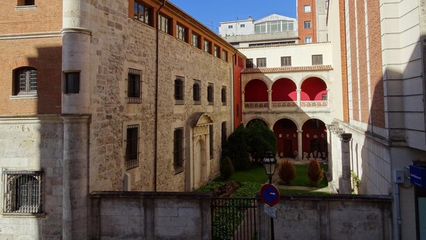 A courtyard with a stone building, arched windows, and a red-roofed structure. - Urban Burgos (Burgos)