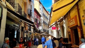 A narrow street with outdoor seating, buildings with balconies, and a clear sky. - Urban Burgos (Burgos)