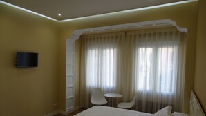 A hotel room with two beds, a TV, a small table, two chairs, and a window with sheer curtains. - Urban Burgos (Burgos)
