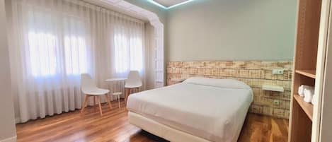 Un dormitorio con cama, una silla, una mesita y una estantería con toallas.