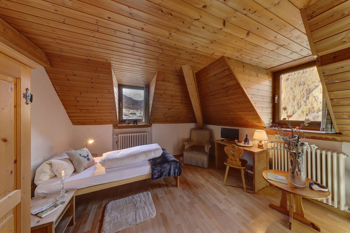 A cozy attic bedroom with a wooden ceiling, a bed, a desk, and a chair.