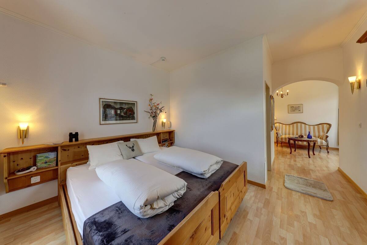 A double bed with a dark headboard, wooden nightstands, and a wall-mounted shelf with books and a pair of binoculars.