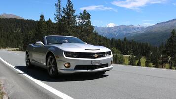 Un Chevrolet Camaro convertible blanco circulando por una carretera con un paisaje montañoso al fondo.