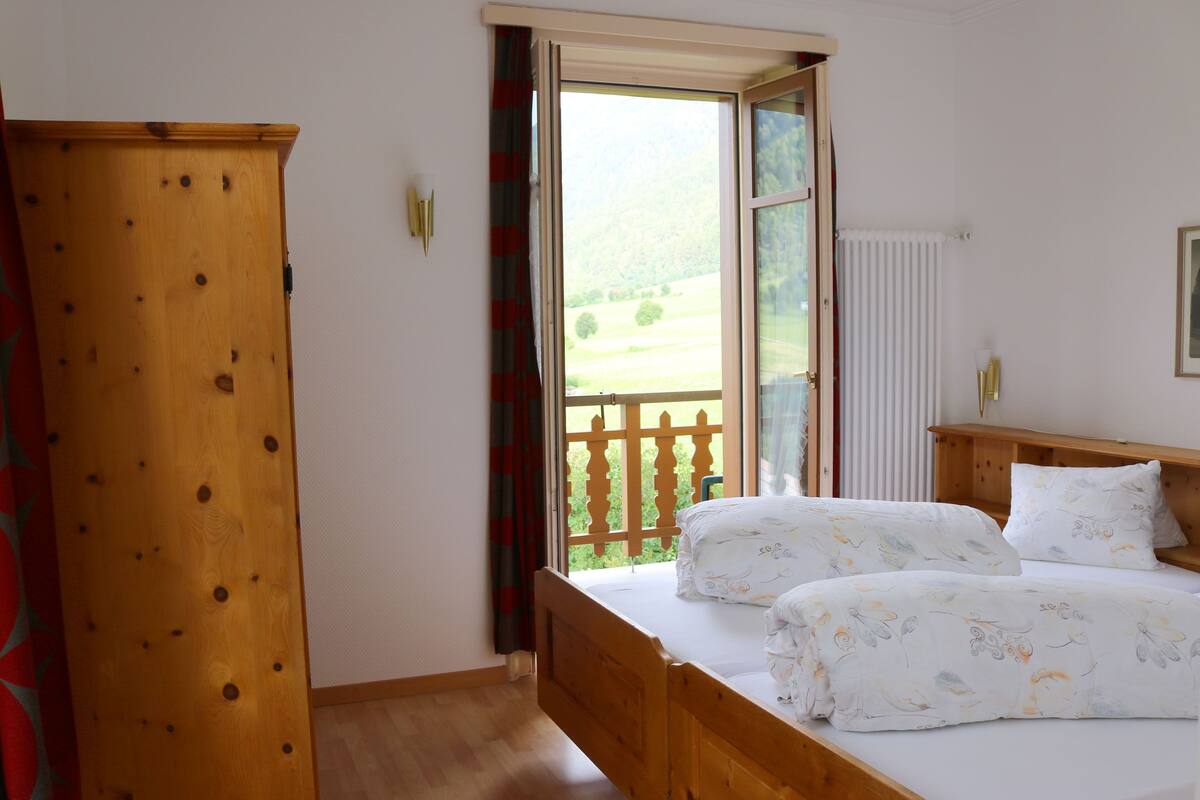 A bedroom with a wooden bed, a window with a view of a green landscape, and a radiator.
