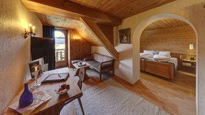 A cozy, wooden-floored room with a loft bed, a seating area with a table, and a dining table with a vase and glasses. - Hotel Restaurant Schweizerhof (Val Muestair)