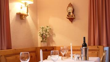 Une table à manger dressée avec des verres à vin, une bougie et une bouteille de vin, et sur le mur, une horloge et des appliques murales.