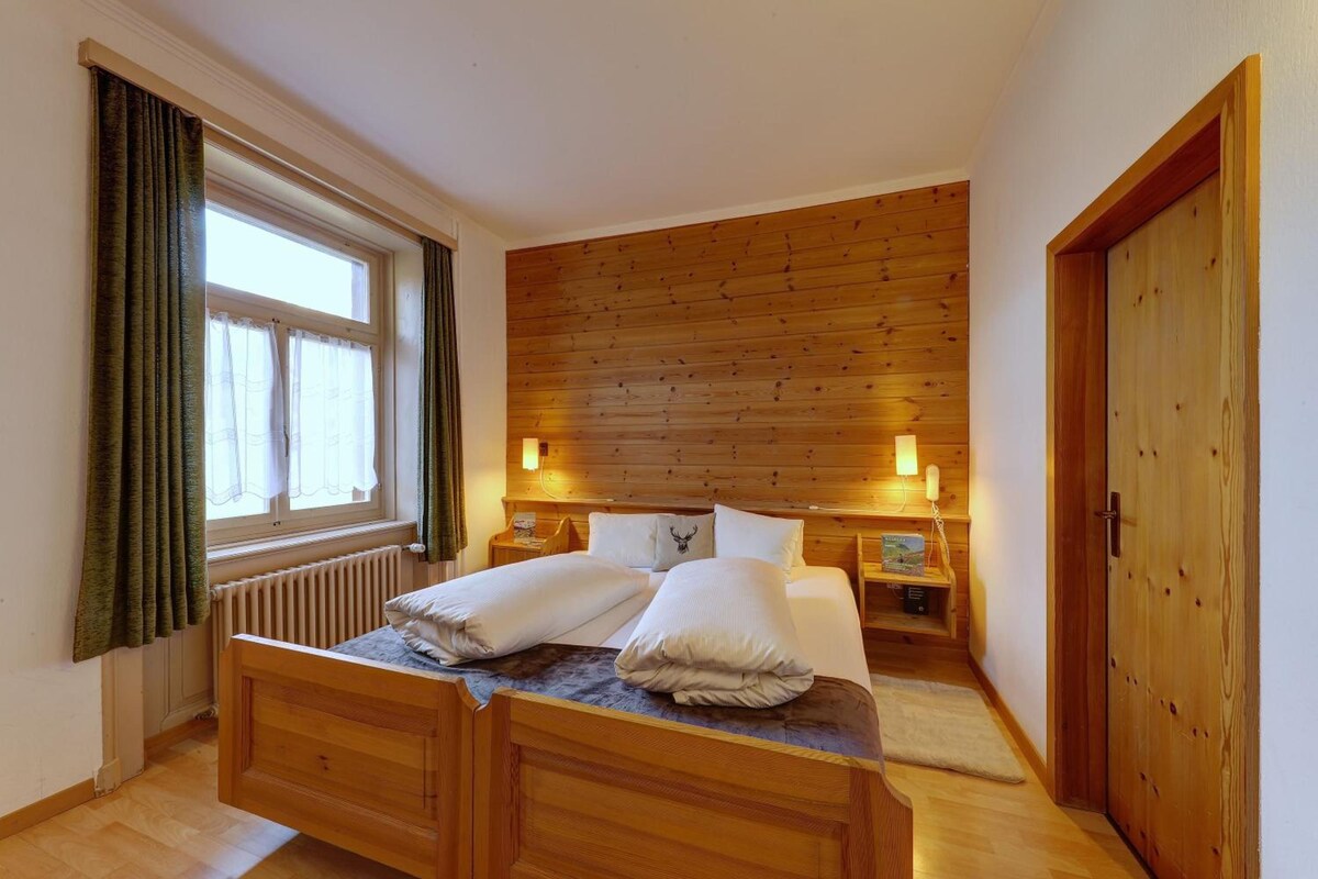 A wooden bed with two pillows, a nightstand with a lamp, and a wooden door.