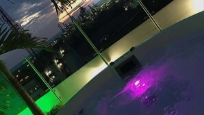 Zona de piscina con vista al horizonte urbano al atardecer, con edificios iluminados y un ocaso.