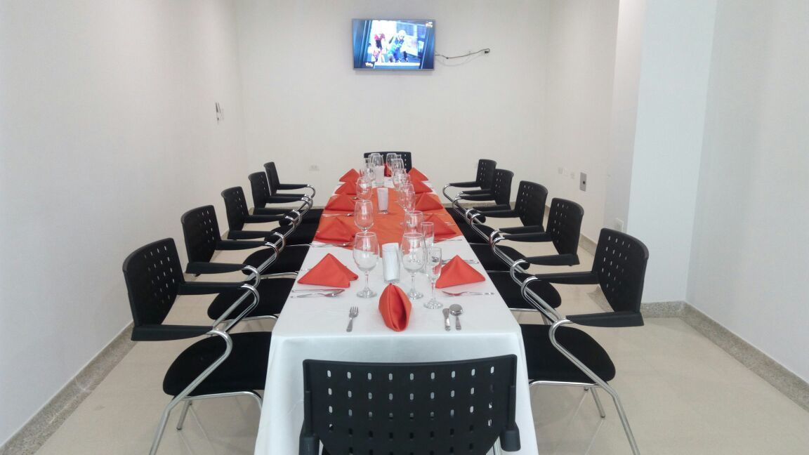 A conference room with a long table set for a meeting, equipped with chairs, a TV screen, and a white tablecloth.