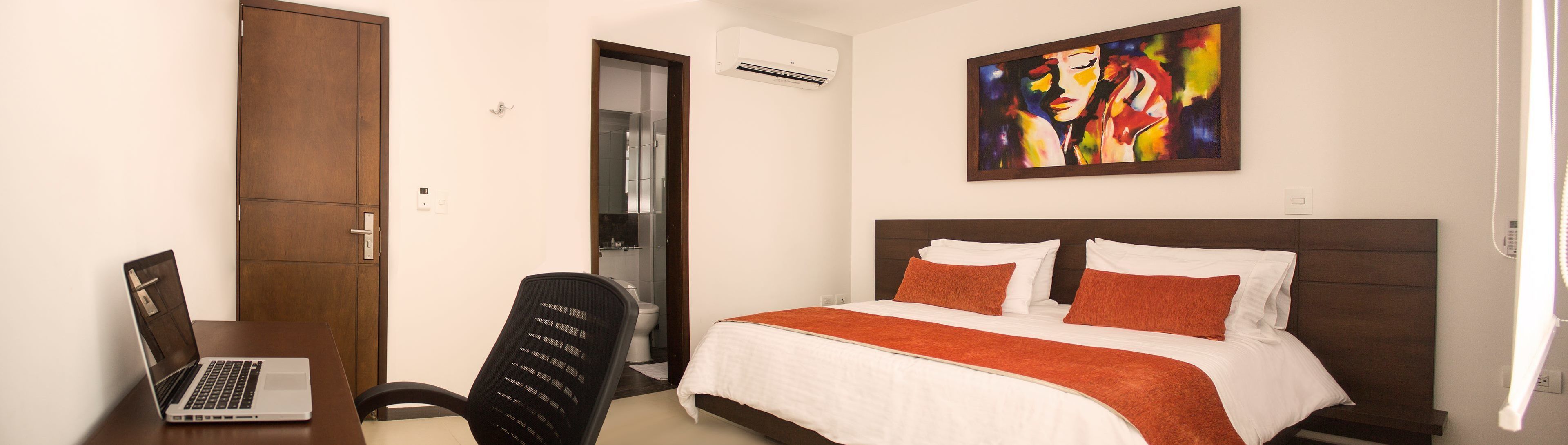 Une chambre d’hôtel équipée d’un lit, d’un bureau avec un ordinateur portable, d’une chaise et d’un appareil de climatisation.