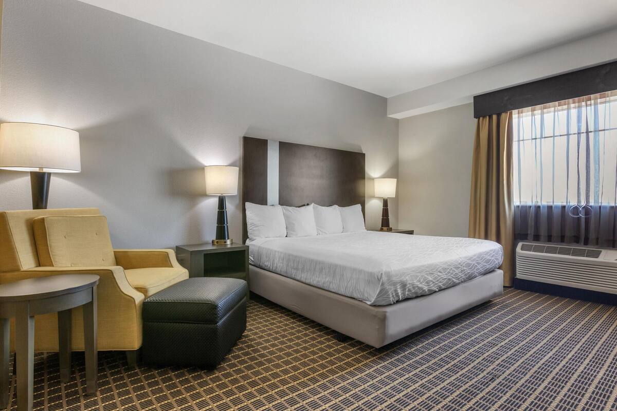 Una habitación de hotel con una cama grande, dos mesitas de noche con lámparas, un sofá, una pequeña mesa y un equipo de aire acondicionado.