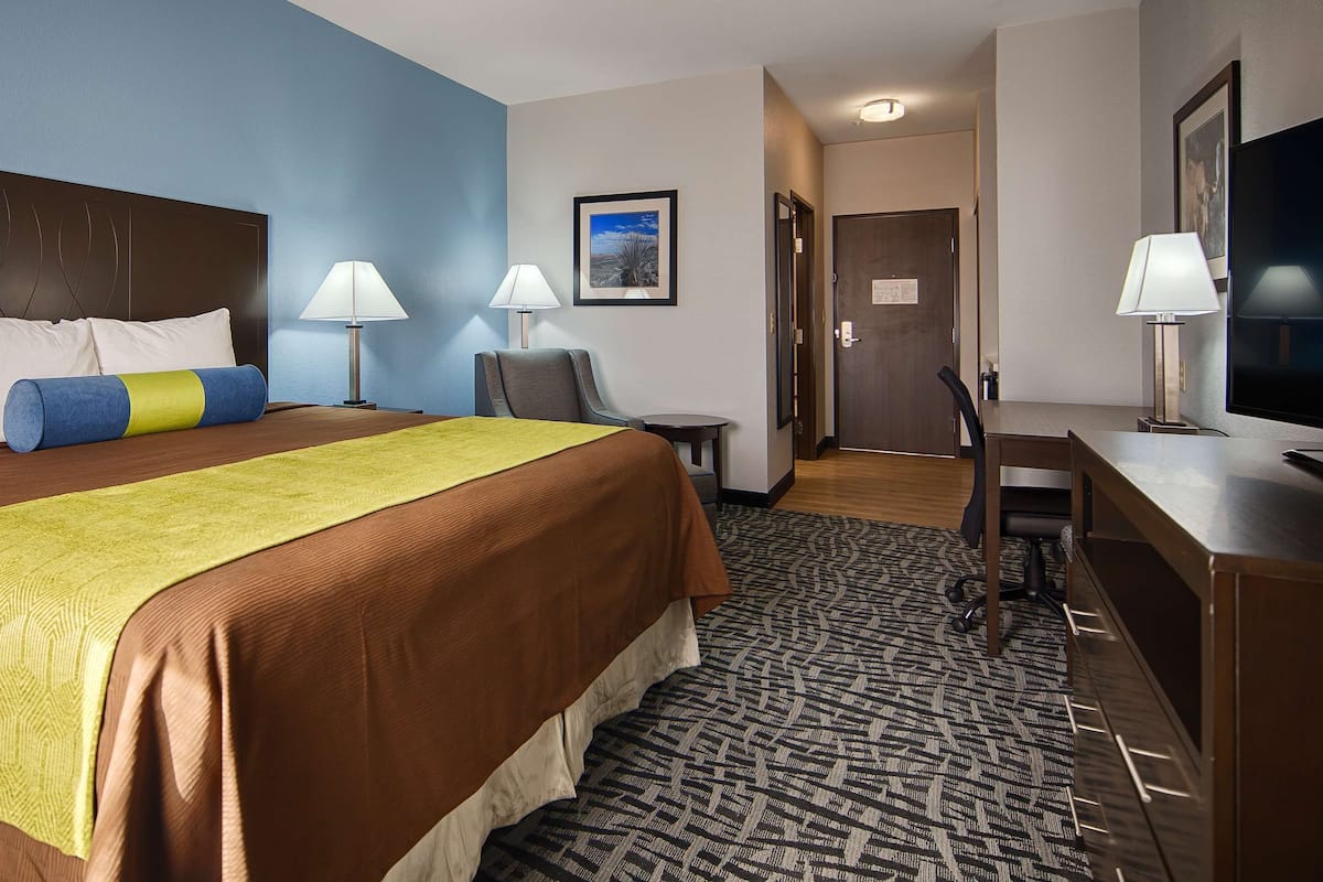 A hotel room with a large bed, two bedside lamps, a desk with a chair, a television, and a framed picture on the wall.