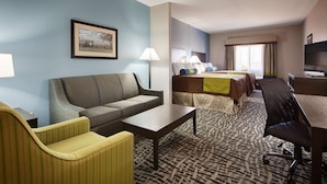 Habitación de hotel con sofá, sillón, escritorio y cama con muchas almohadas.