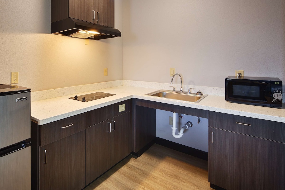 A modern kitchen with dark wood cabinets, a stainless steel refrigerator, a microwave, and a sink with a faucet.