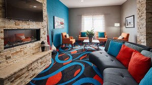 Una sala de estar moderna con chimenea de piedra, sillones naranja, un sofá gris con cojines de colores y una alfombra con motivos vivos.