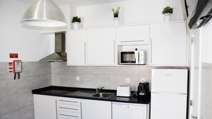 Una cocina moderna con armarios blancos, un lavamanos de acero inoxidable, un microondas, un tostador y un refrigerador.