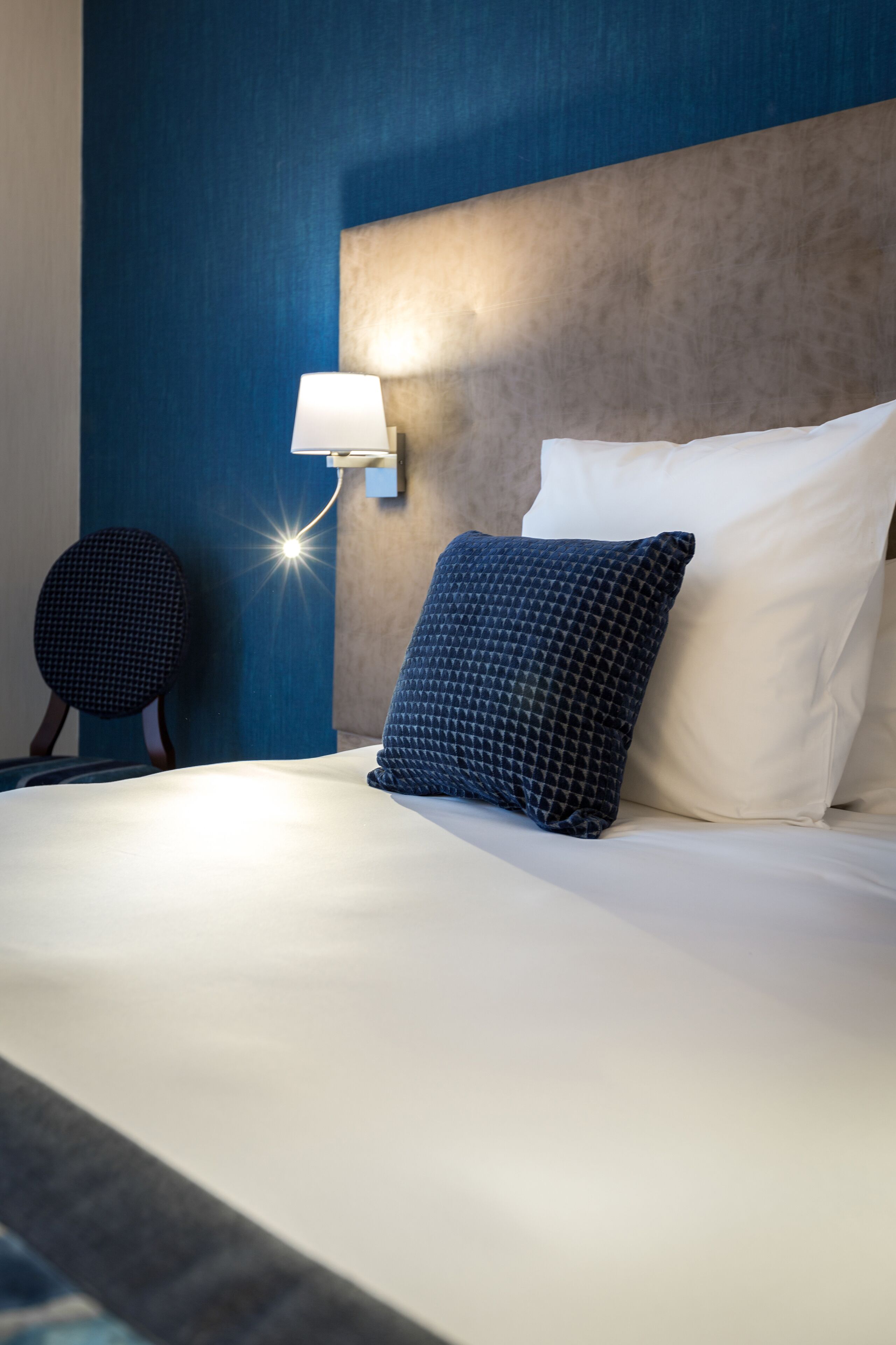 A hotel room with a bed, a wall-mounted lamp, and a round chair.