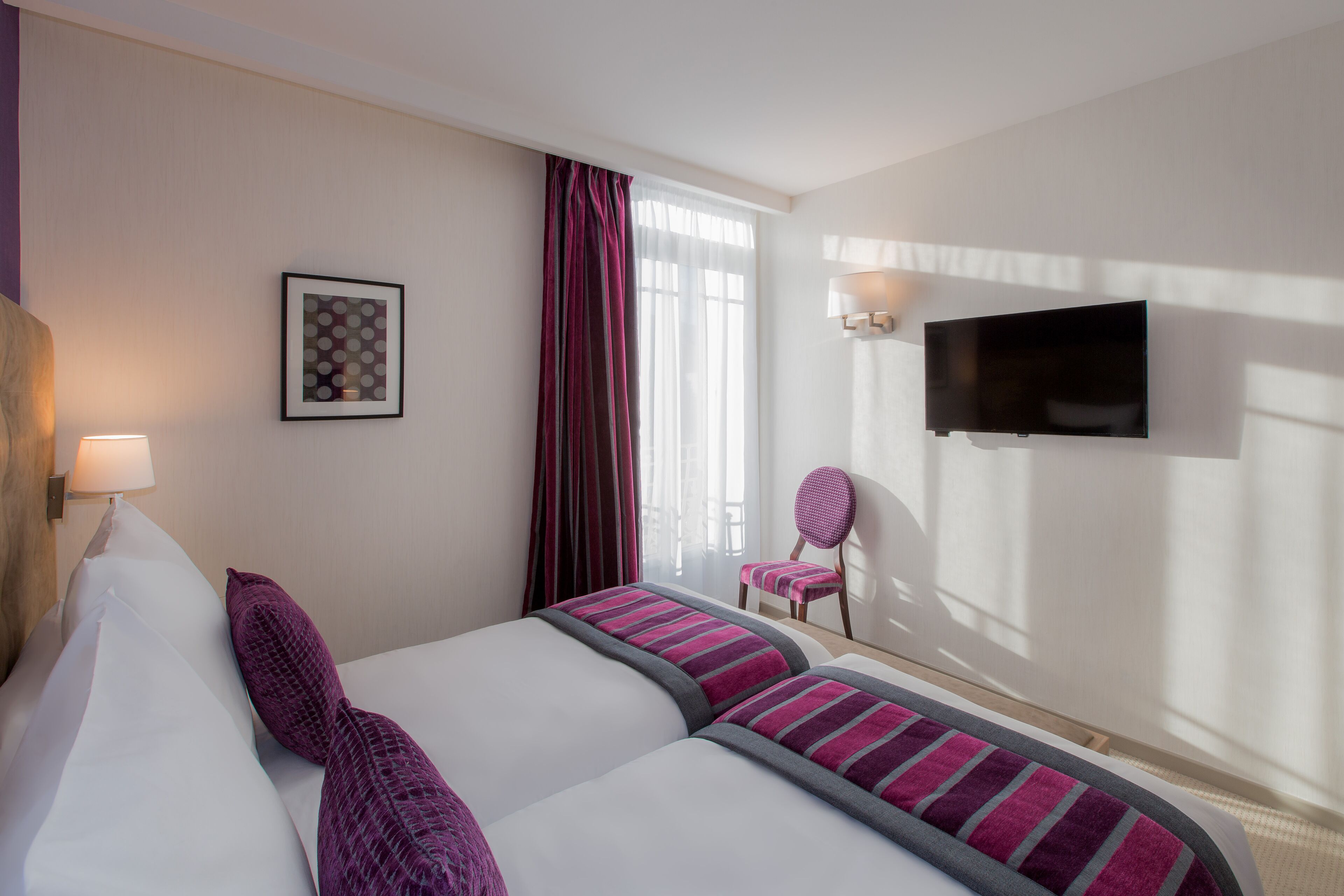 Habitación de hotel con dos camas, televisión, una silla y ventana con cortinas.
