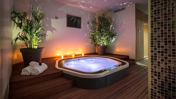 Un bain à remous avec une terrasse en bois, deux plantes en pot et un tableau accroché au mur.
