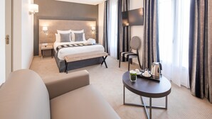 Une chambre d’hôtel moderne dotée d’un grand lit, de tables de chevet, d’un canapé, d’une petite table avec une bouilloire et d’un téléviseur fixé au mur.