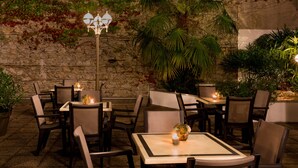Un espace extérieur aménagé pour les repas, avec des murs en pierre, des tables, des chaises et des plantes en pot.