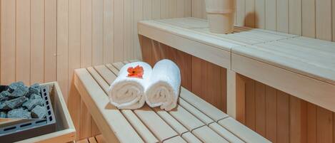 Una sauna de madera con bancos, toallas y un cubo.