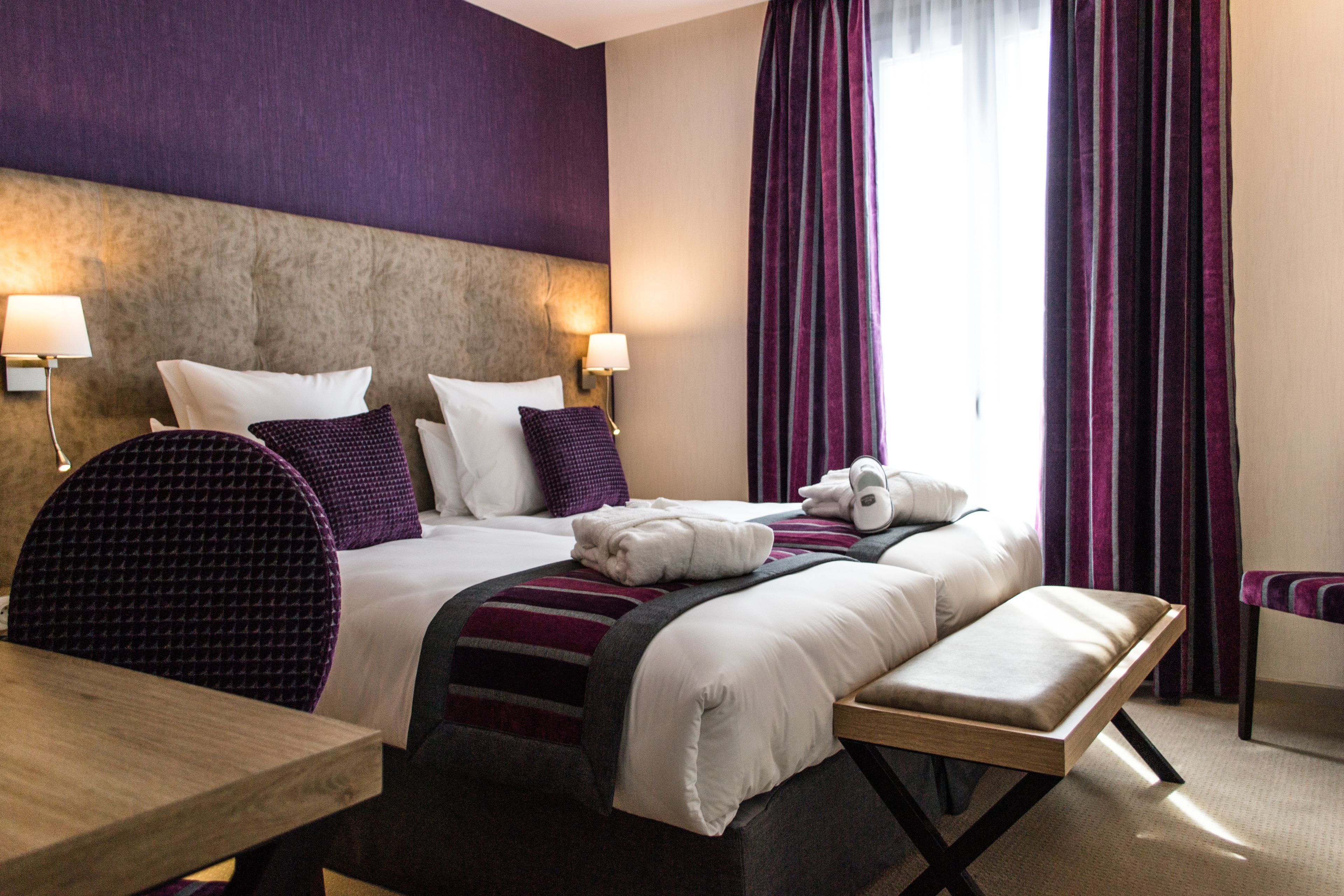 A hotel room with a large bed, two bedside lamps, a bench, and a chair.