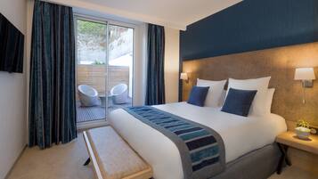 A hotel room with a large bed, a bedside table with a lamp, a bench, and a view of the outdoors through a sliding door.