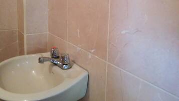 Un baño con lavamanos blanco, un espejo y paredes cubiertas de baldosas color beige.