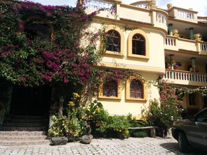 Un edificio de varios pisos con balcones, ventanas de arco y un acceso empedrado con escalones.