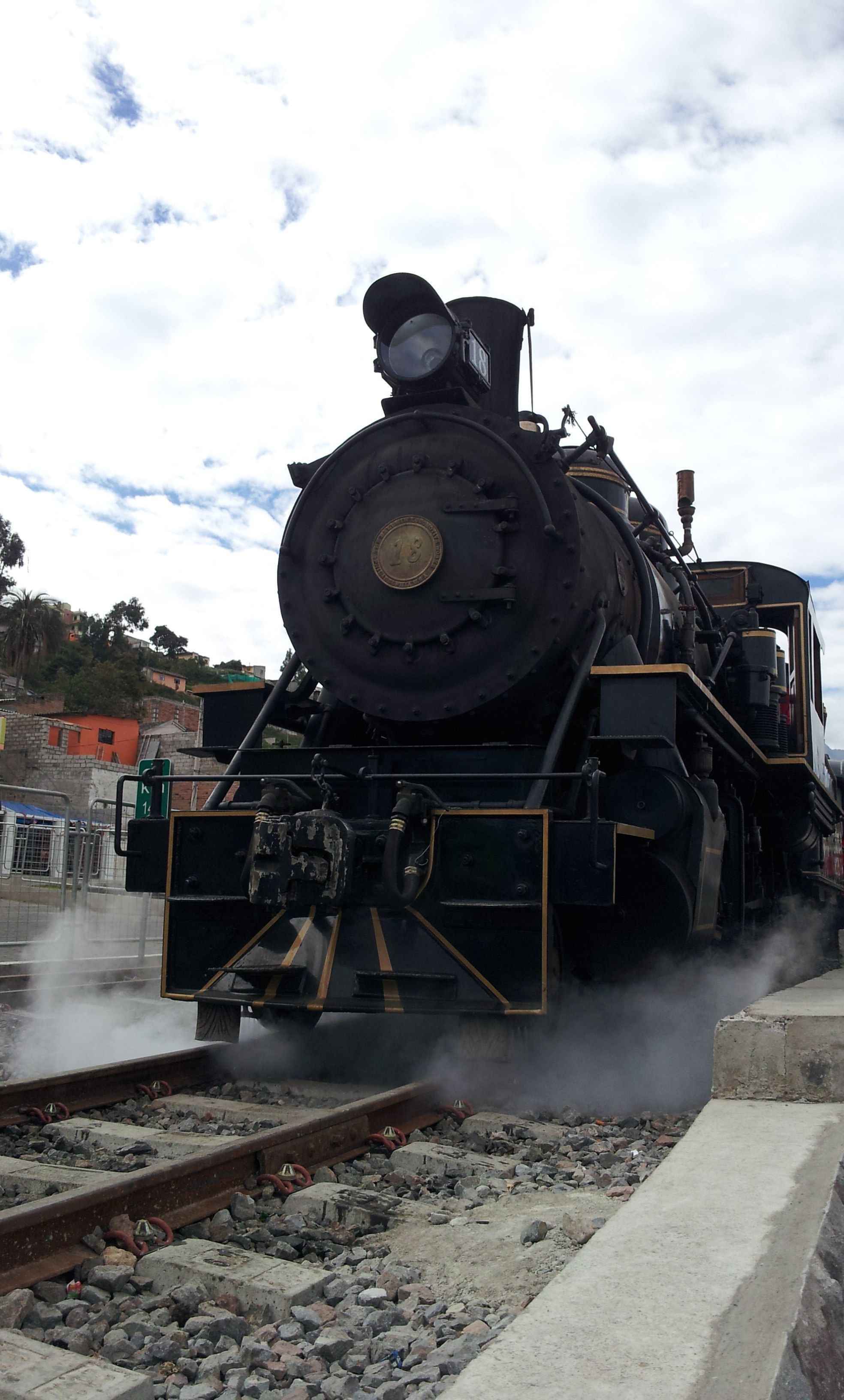 Una locomotora de vapor con una rueda delantera grande y un farol, emitiendo vapor por el frente.