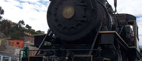 Una locomotora de vapor con una rueda delantera grande y un farol, emitiendo vapor por el frente.