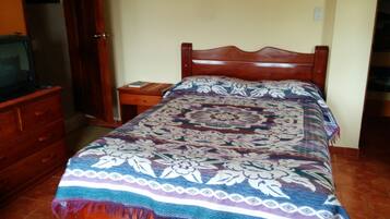 A bedroom with a wooden bed, a nightstand, a dresser, and a television on a wooden cabinet.