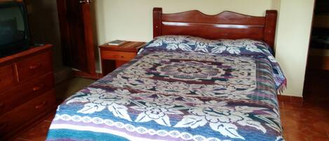 A bedroom with a wooden bed, a nightstand, a dresser, and a television on a wooden cabinet.