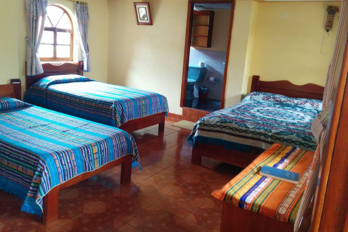A room with two beds, a window with curtains, a wooden door, and a small mirror on the wall.