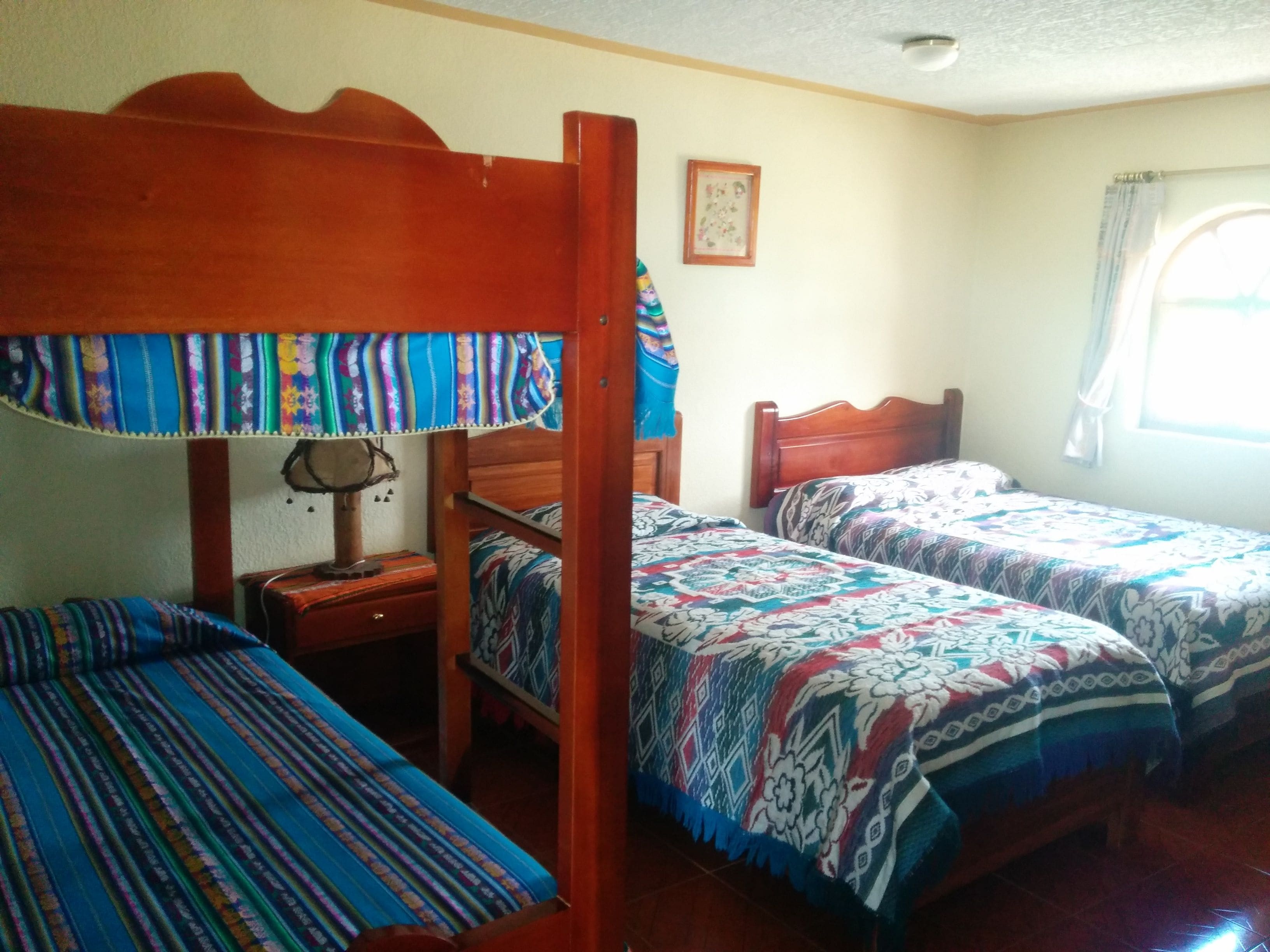 Una habitación con dos camas de madera, una mesita de noche de madera y una ventana con cortinas.