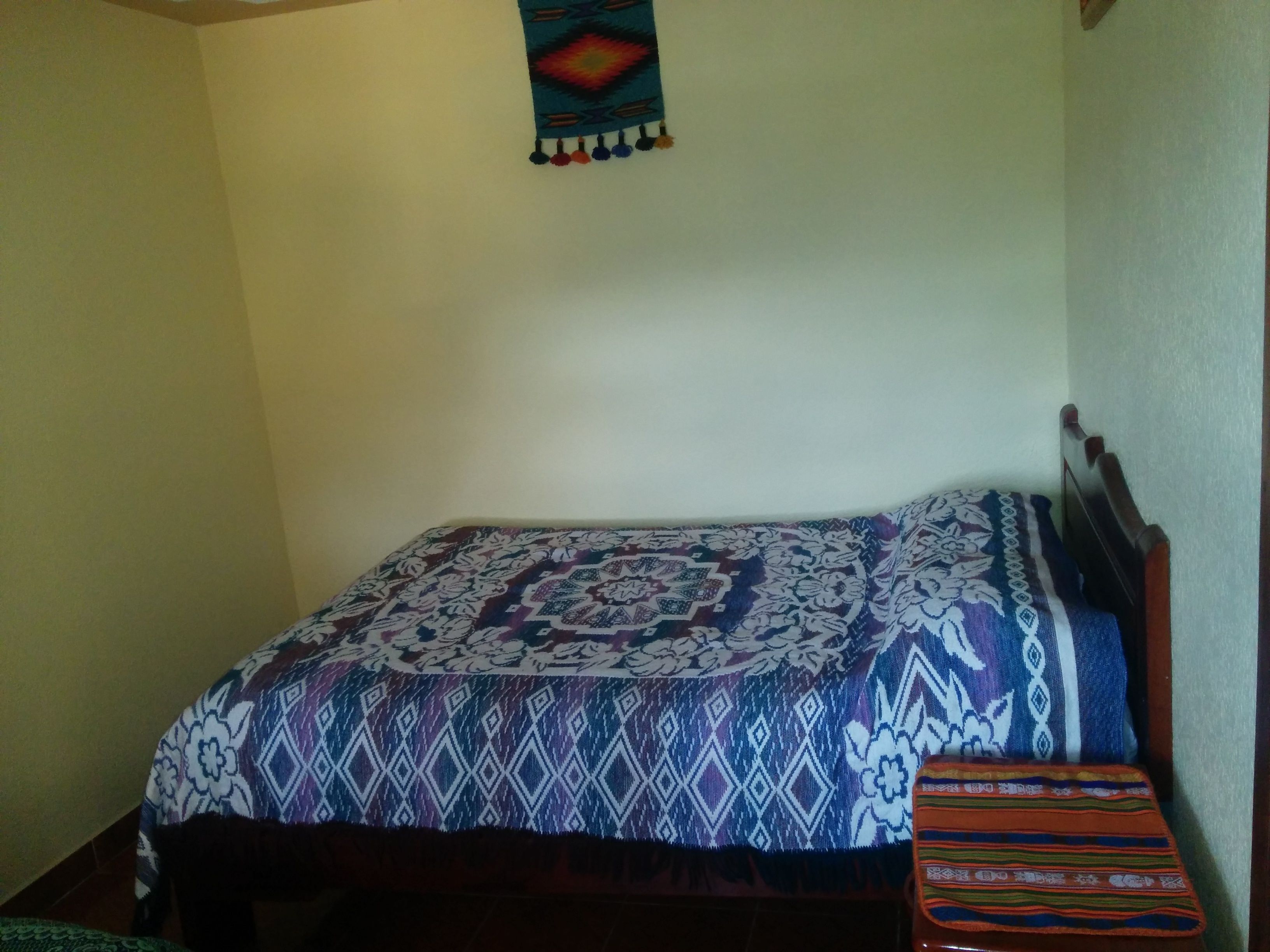 Una cama pequeña y bien hecha, con una colcha estampada y una manta colorida al lado.