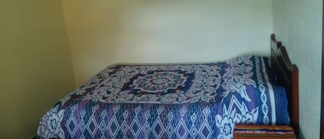 Una cama pequeña y bien hecha, con una colcha estampada y una manta colorida al lado.
