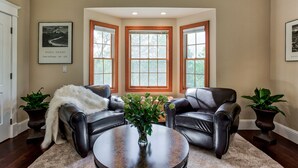 A living room with a brown leather sofa, a coffee table with a vase of flowers, and a large window with wooden frames. - Hope Inn Redding (Redding)