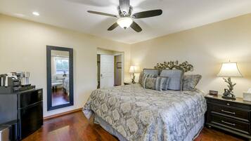 A bedroom with a bed, a ceiling fan, a nightstand, a lamp, a dresser, and a mirror.