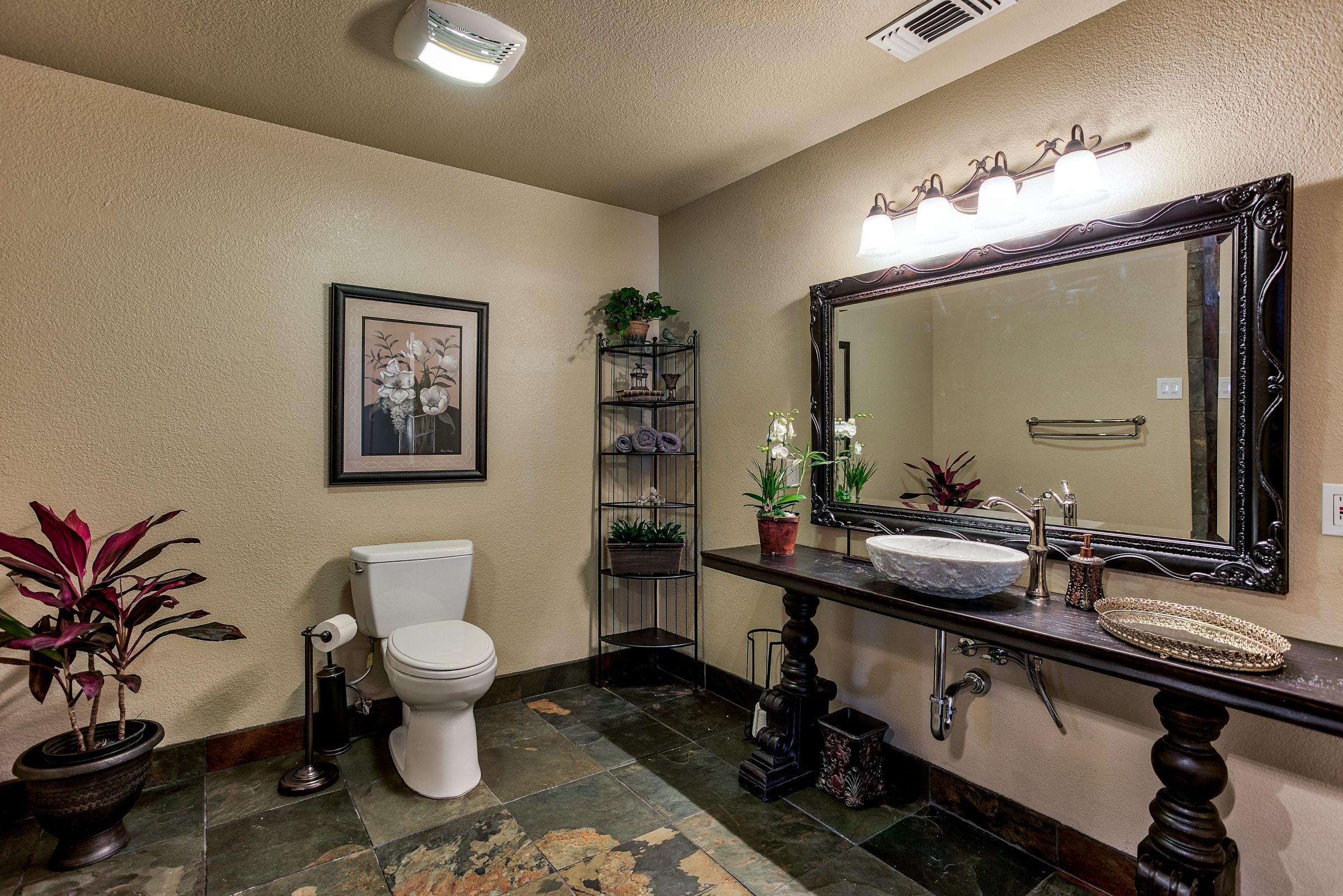 A bathroom with a white toilet, a sink with a large mirror, and shelves with potted plants.