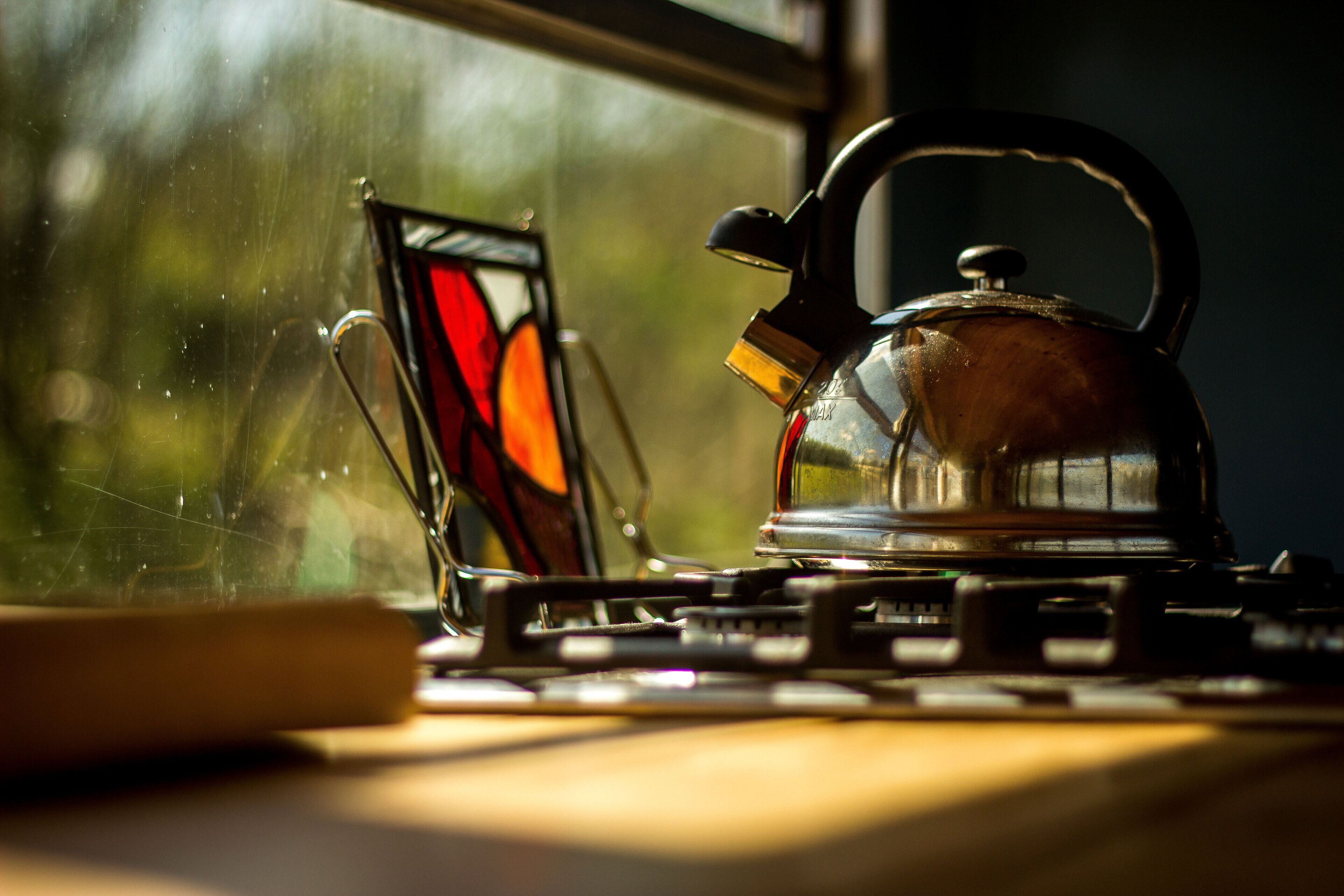 A kettle on a stove with a window in the background.